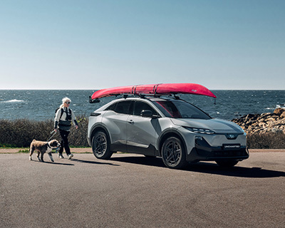 Subaru Uncharted med kajakker på taget parkeret ved havet med en person og hund.