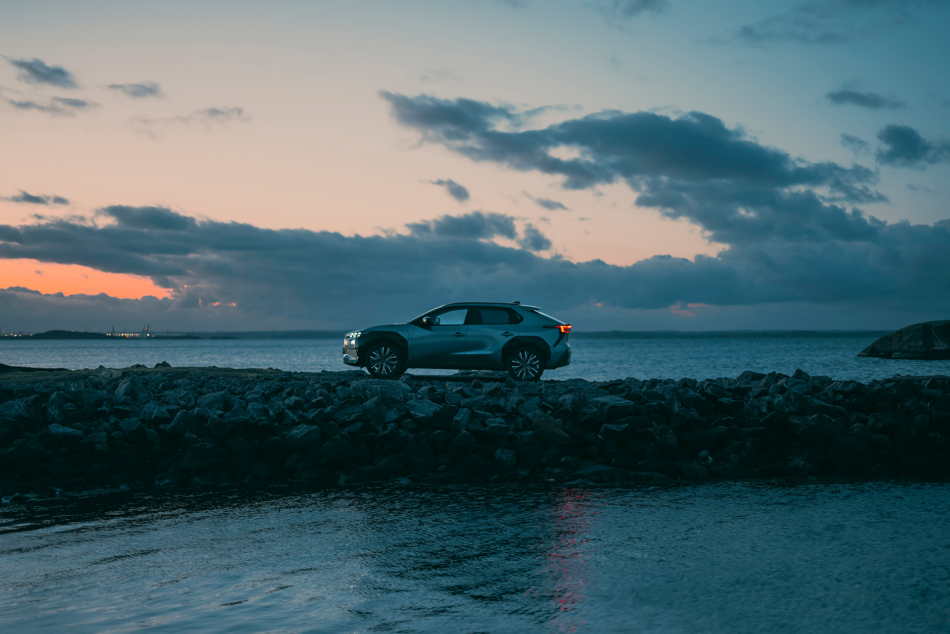 Subaru Solterra parkeret ved en klippekyst ved havet i solnedgangen.
