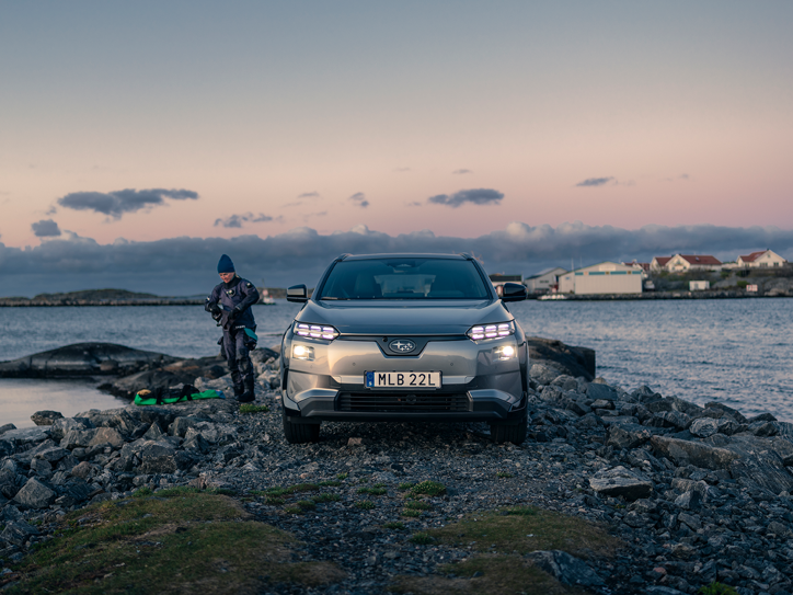 Subaru Solterra på en klippekyst med en person i dykkerudstyr ved havet.
